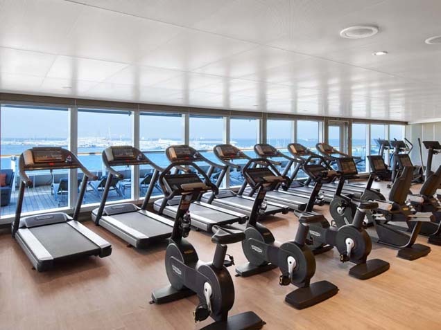 Fitness center - rows of treadmills and cycling machines with mirrored walls and hardwood flooring.